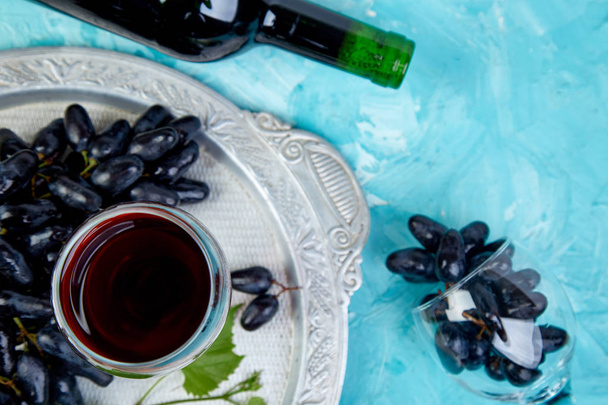 Κόκκινο κρασί έννοια με μπουκάλι, ποτήρι και σταφύλια σε ασημένιο δίσκο σε μπλε φόντο, το top view, επίπεδη θέσει. Κρασί κεφαλίδα εικόνας. Wineglasses - Φωτογραφία, εικόνα