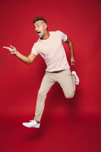 Full length photo of adult man in striped t-shirt running and screaming isolated over red background - Fotó, kép