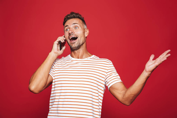 Portrait of an excited man standing over red background, talking on mobile phone - Foto, Bild