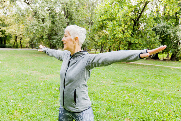 Zdrowe średnim wieku Kobieta w sportowej robi ćwiczenia rozciągające w przyrodzie - Zdjęcie, obraz