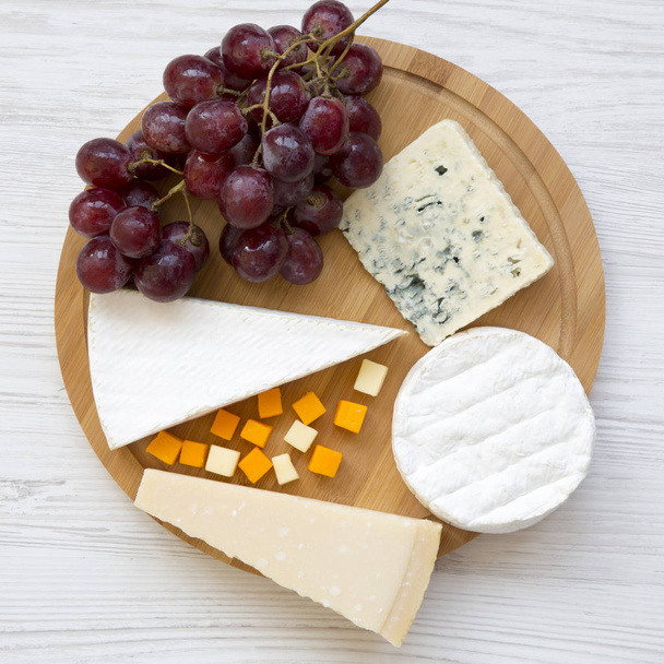 Dégustation de différents types de fromage avec des raisins sur une planche ronde en bois, vue aérienne. De la nourriture pour le vin. Couché plat, d'en haut, vue de dessus
. - Photo, image