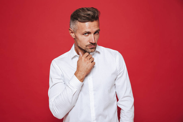 European guy with stubble in white shirt looking aside isolated over red background - Foto, imagen