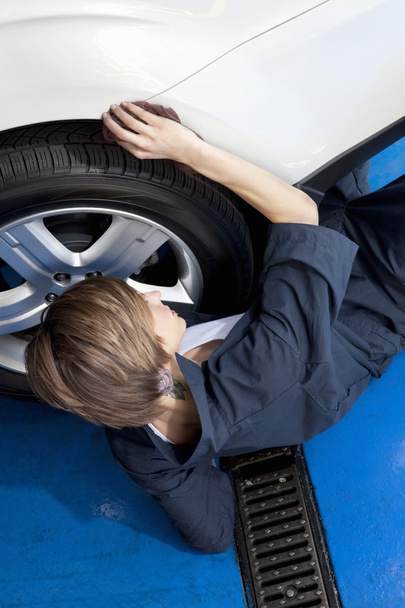 hoge hoekmening van jonge mechanic liggend op vloer werken op auto band in garage - Foto, afbeelding