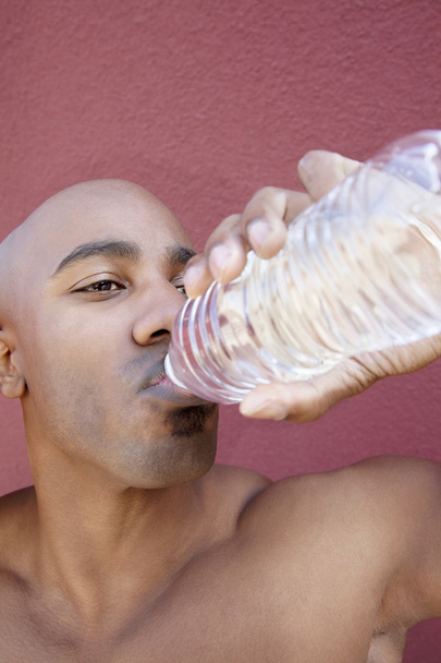 Young African American man drinking water from bottle over colored background - Valokuva, kuva