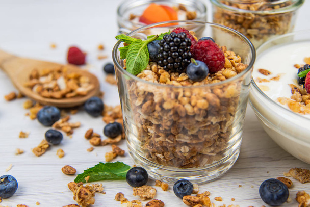 Jars full with granola, yogurt and fresh berries and wood spoon full whit granola, close-up, selective focus - Φωτογραφία, εικόνα