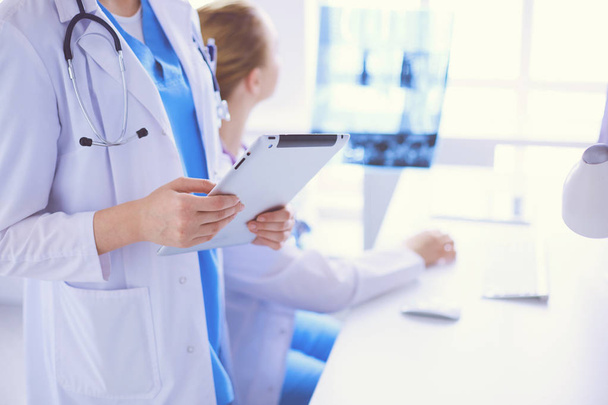 Nahaufnahme von Arzt mit Tablet und Kollege mit Röntgenbild im Hintergrund. - Foto, Bild