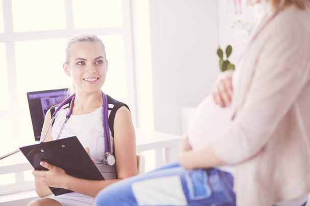 Doctora joven con estetoscopio y tableta que habla con una mujer embarazada en el hospital. - Foto, imagen