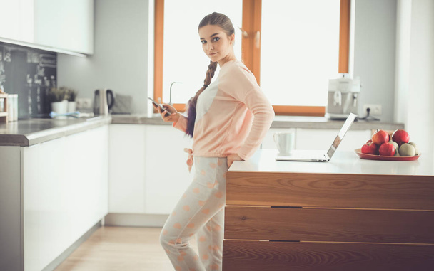Woman using mobile phone standing in modern kitchen. - Foto, afbeelding