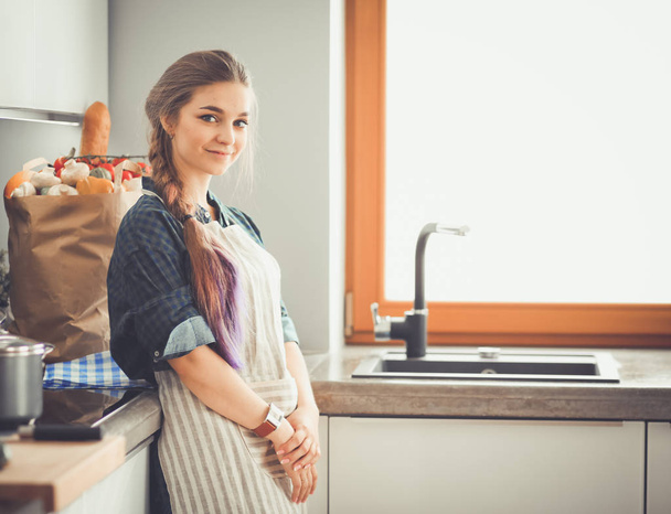 Mutfakta sobanın yanında duran genç bir kadın. . - Fotoğraf, Görsel