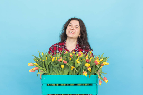 Bella scatola di tenuta giardiniere femminile con tulipani su sfondo blu
 - Foto, immagini