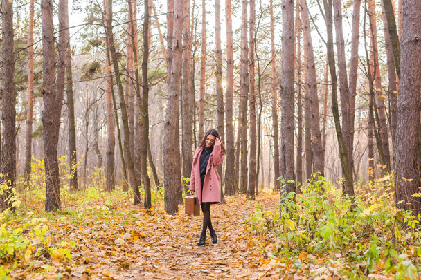 Autumn, nature and people concept - Portrait of beautiful smiling woman with brown suitcase walking in fall - Photo, Image