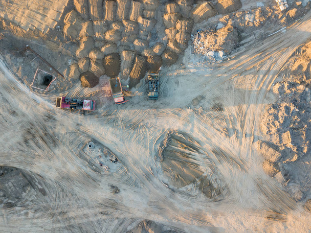 Aerial view of three multi-colored dump tip trucks unloading in a designated place at a construction site, soil poured out from a quarry poured out of a quarry, around a large number of sand mounds - Photo, Image