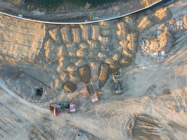 Luchtfoto van drie multi-gekleurde dump tip vrachtwagens lossen op een aangewezen plaats op een bouwplaats, bodem uitgestort uit een steengroeve gegoten uit een steengroeve, rond een groot aantal zand heuvels - Foto, afbeelding