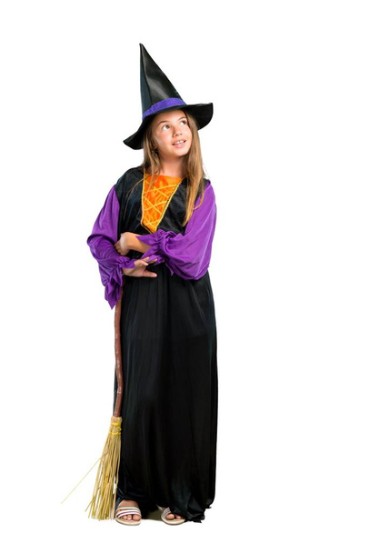 Полнометражный снимок маленькой девочки, одетой как ведьма на праздники Хэллоуина стоять и смотреть вверх изолированы на белом
 - Фото, изображение