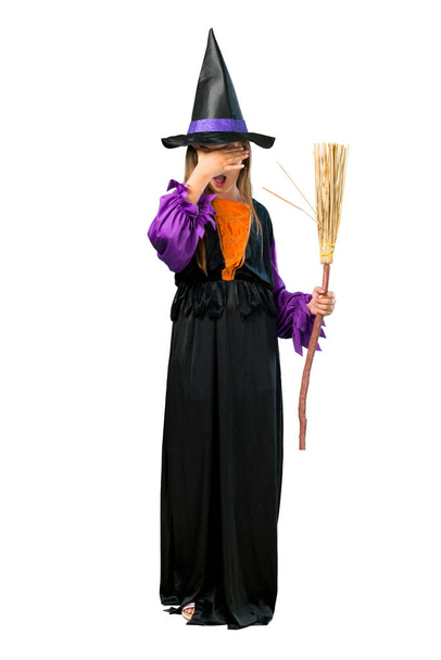 Um tiro de comprimento total de uma menina vestida como uma bruxa para feriados de Halloween cobrindo os olhos por mãos isoladas em branco
 - Foto, Imagem