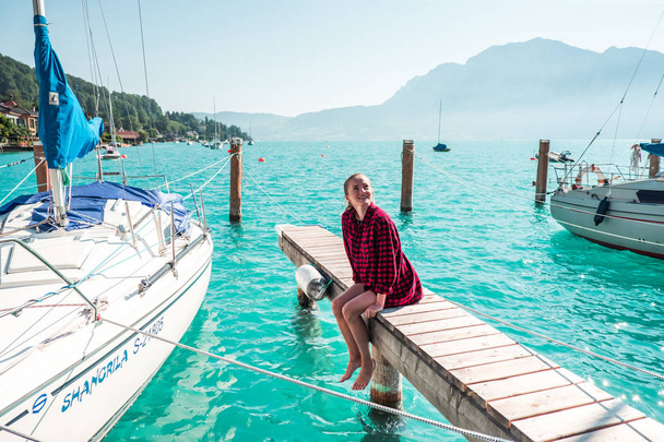 Young woman sitting on wooden pier on pure lake surrounded with mountains, in Austrian Alps - Photo, Image