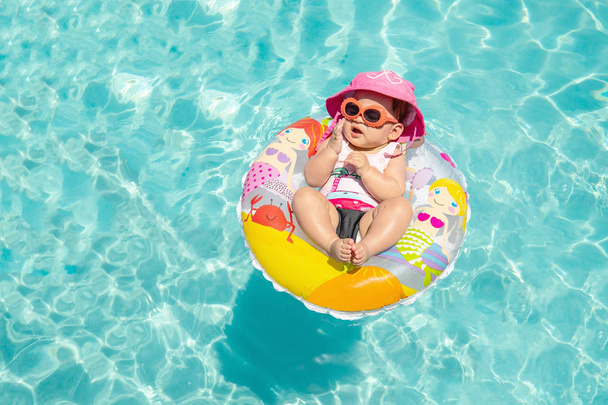 Schattige babymeisje In zonnebril drijvend op tropische blauw Water - Foto, afbeelding