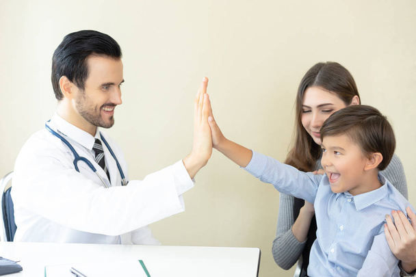 Little boy with his mother at a doctor on consultation. Male doctor is smiling and giving high five to little boy after medical checkup.Concept of healthcare, medical treatment and insurance. - Фото, зображення