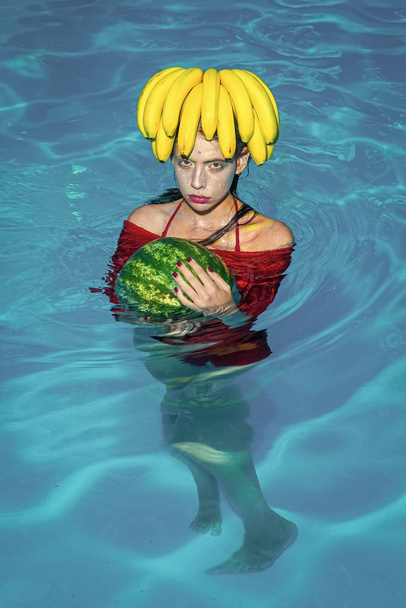 Woman swim in a pool with tropical fruit of banana and watermelon. - Foto, Imagem