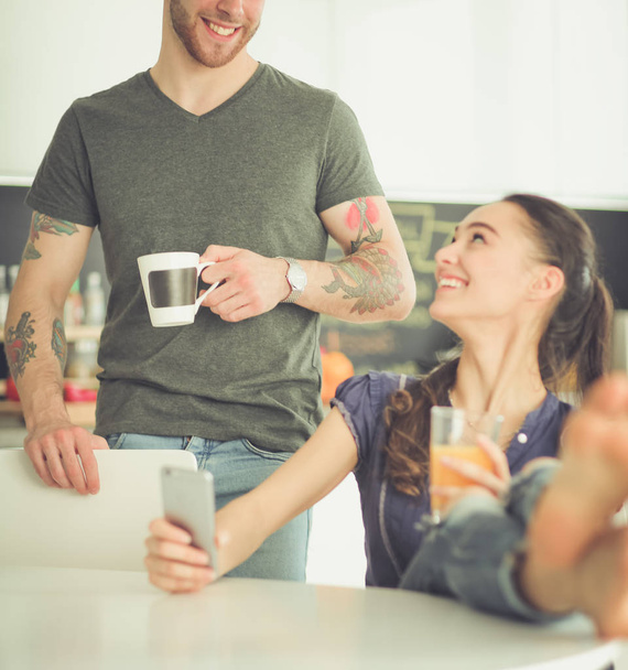 Happy couple using smartphone sitting in kitchen - Φωτογραφία, εικόνα
