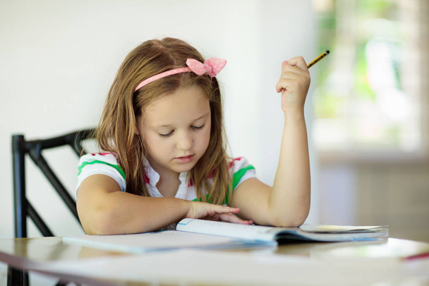 Cute dziewczynka odrabiania lekcji, czytanie książki, kolorowanki, malowanie i pisania. Dzieci farby. Dzieci rysują. Dziecko robi matematyki papieru dla szkoły z książek w domu. Studenci uczą się pisać i czytać.  - Zdjęcie, obraz