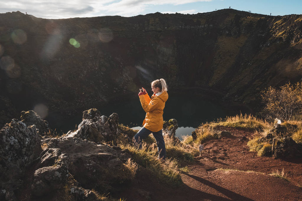 Nainen seisoo kalliolla ja katselee Alppien järvi, Islanti
. - Valokuva, kuva