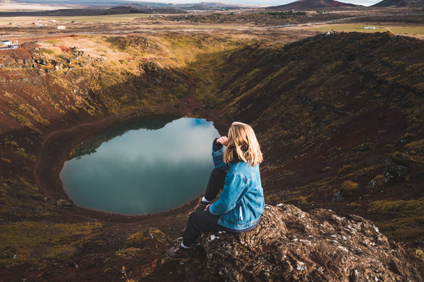 woman sitting on rocky cliff and looking at alpine lake, Iceland. - Photo, Image