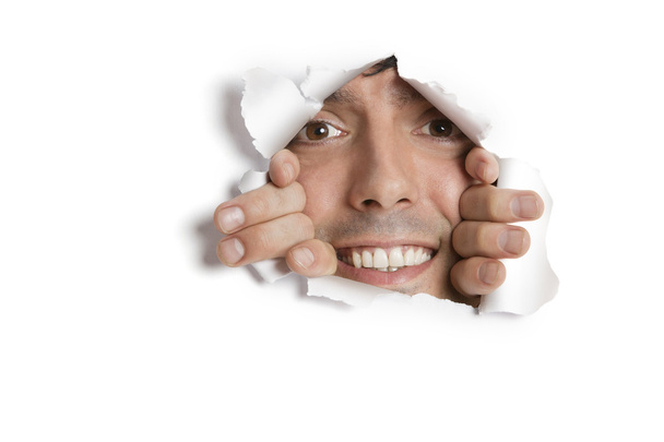 Portrait of a happy young Hispanic man peeking from ripped paper hole - Foto, Imagen
