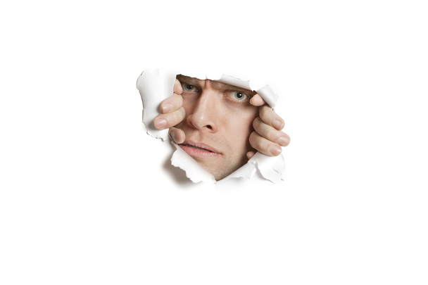 Portrait of a mid adult Caucasian man peeking from ripped white paper hole - Fotó, kép