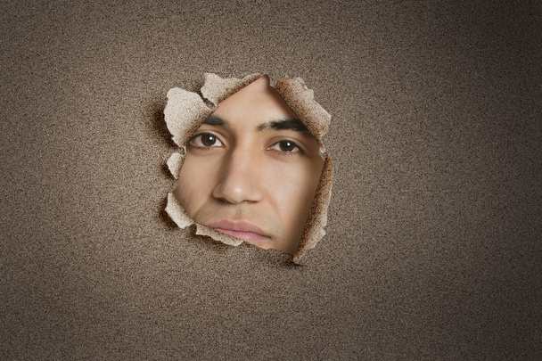 Portrait of a young Indian man peeking from ripped paper hole - Foto, Imagen