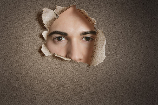 Portrait of a young Caucasian man peeking from ripped paper hole - Foto, Imagen