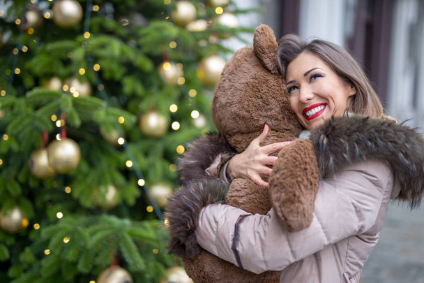 Красивая молодая женщина обнимает плюшевого медведя подарок на Рождество на улице
 - Фото, изображение