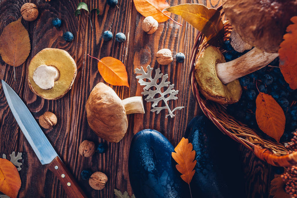 Porcini mushrooms in basket with berries and nuts on wooden table. Autumn harvest with shoes. Gathered in forest fall crop - Фото, изображение