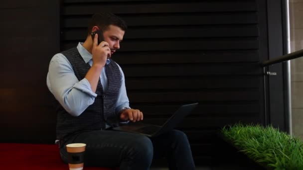 hombre de negocios freelancer que trabaja en el ordenador portátil con diagramas en la pantalla en la cafetería, beber café y hablar por teléfono. Seguimiento y disparo revelador
 - Imágenes, Vídeo