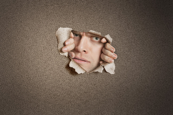 Portrait of a mid adult Caucasian man peeking from ripped white paper hole - Foto, Imagem