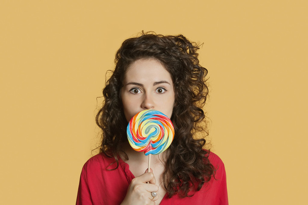 Portrait of a young woman holding lollipop in front of face over colored background - Foto, imagen