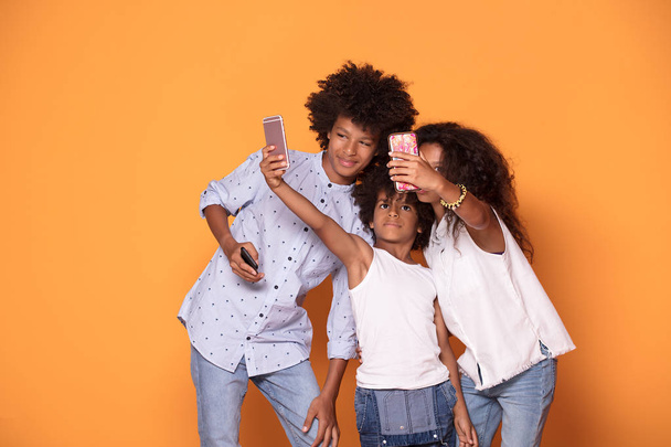 Feliz sonriendo tres afro niños en ropa colorida posando juntos, sonriendo, tomando selfie por teléfono móvil
. - Foto, Imagen