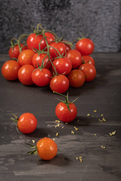 Małe czerwone pomidory cherry na tle rustykalnym. Wiśniowe pomidory na winorośli witb bazylia pozostawia. - Zdjęcie, obraz