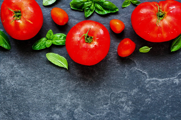 Fresh tomato and basil leaves on dark copy space background close up. Flat lay, top view - Zdjęcie, obraz