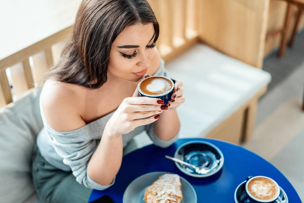 Close up of young beautiful woman holding cup of coffee and enjoying its aroma. - Foto, imagen