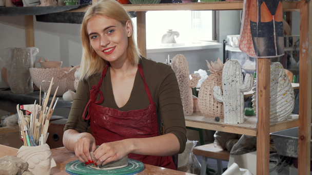 Gorgeous young woman smiling while working with clay at the workshop - Photo, Image