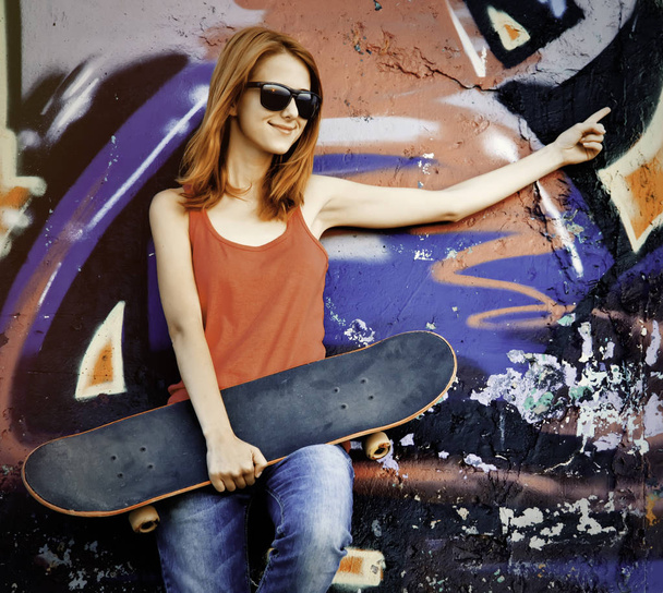 Chica de estilo con monopatín cerca de la pared de graffiti
. - Foto, Imagen