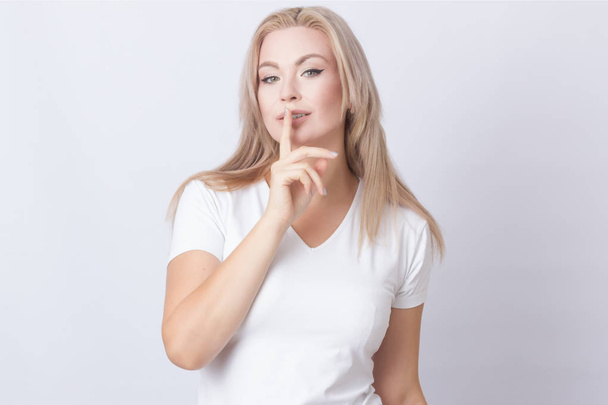 Image of beautiful blonde woman holding finger near her lips. Isolated over grey background - Фото, зображення