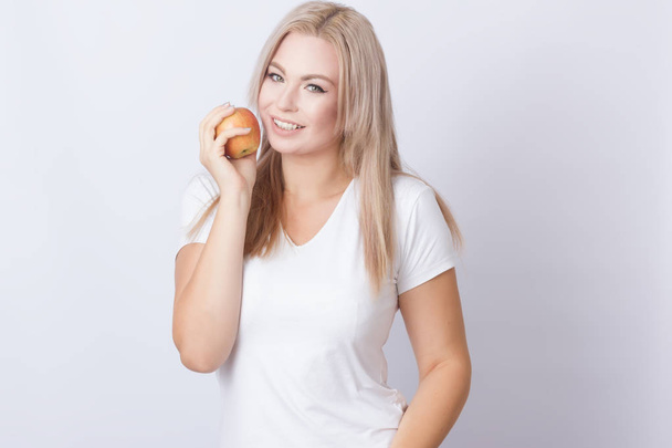 Photo portrait of pretty young blonde longhair woman standing over grey background holding apple in her hands - Photo, image