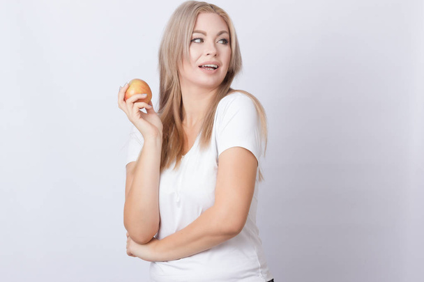 Photo portrait of pretty young blonde longhair woman standing over grey background holding apple in her hands - Photo, image