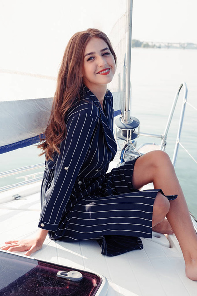 Attractive girl on a yacht at summer day. Close up of fashion portrait of stunning romantic woman posing yacht. Wearing an elegant dress, summer outfit. Blue sky. sunset - Photo, image