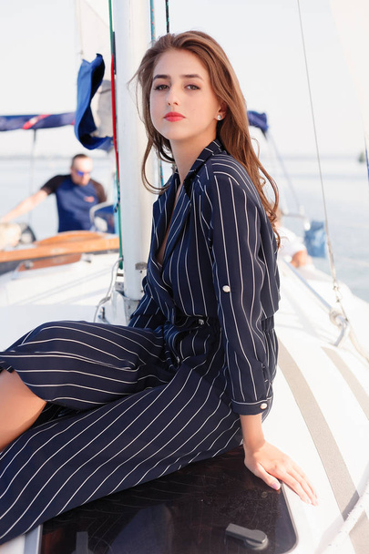 Attractive girl on a yacht at summer day. Close up of fashion portrait of stunning romantic woman posing yacht. Wearing an elegant dress, summer outfit. Blue sky. sunset - 写真・画像