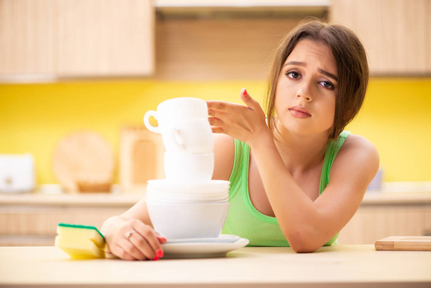 Νεαρή γυναίκα που καθαρίζει και πλένει πιάτα στην κουζίνα - Φωτογραφία, εικόνα