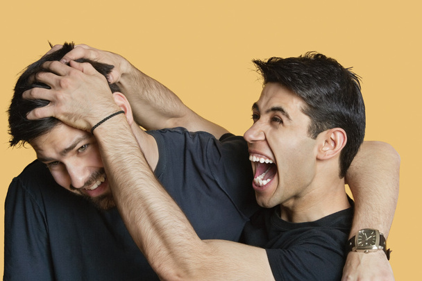 Young male friends playfighting over colored background - Fotoğraf, Görsel