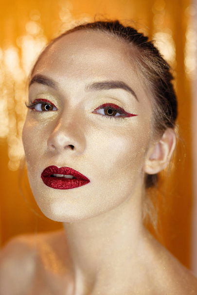 Magic Girl Portrait in Gold. Golden Makeup, close-up portrait in studio shot, color. Beauty Model Girl with perfect bright make-up, red lips, golden maroon jewellery. Sexy lady makeup Holiday party. - Valokuva, kuva